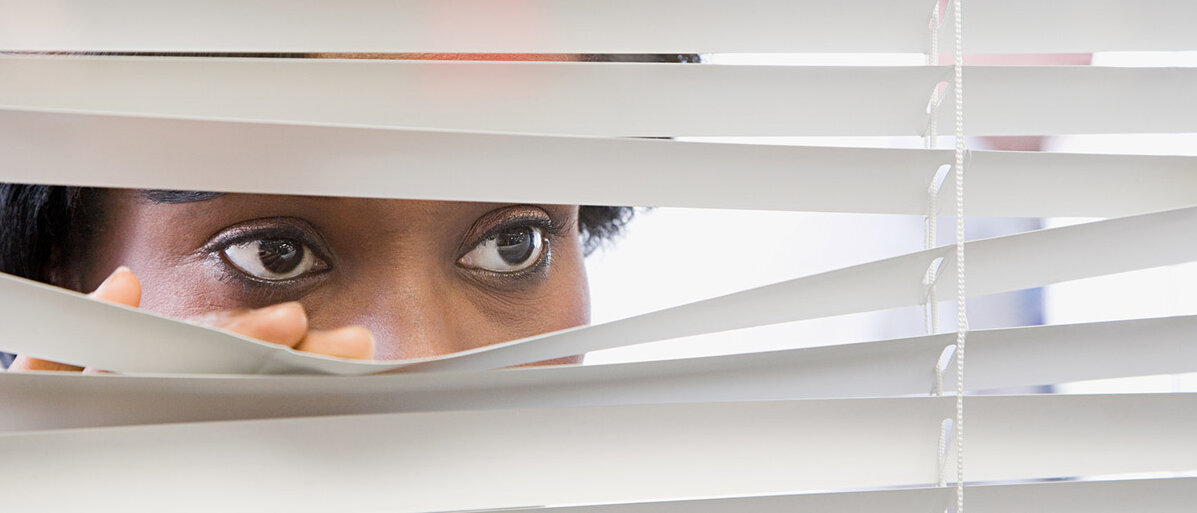 Frau blickt durch Jalousie