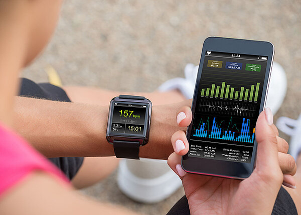  Frau checkt Fitness-App auf Handy und Smartwatch 