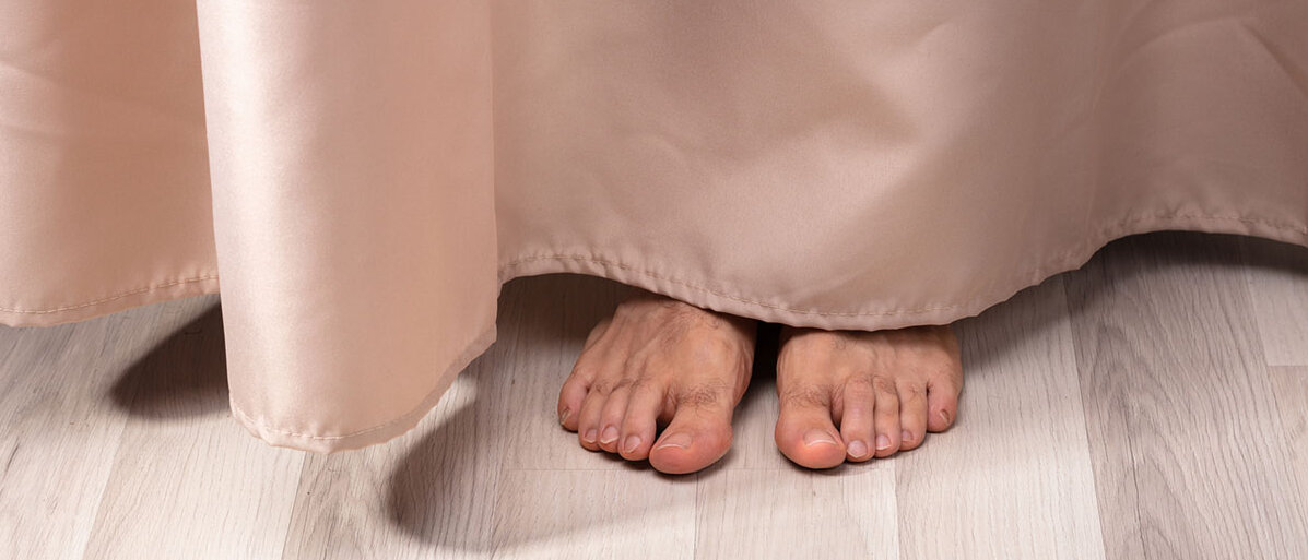Mann versteckt sich hinter Vorhang. Zu sehen sind nur seine blanken Füße.