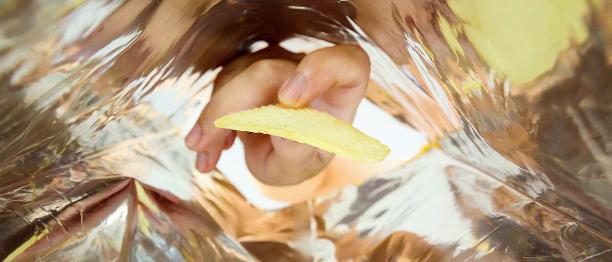 Blick vom Boden einer Tüte Chips in Richtung Öffnung: Eine Hand greift nach dem letzten Chip.