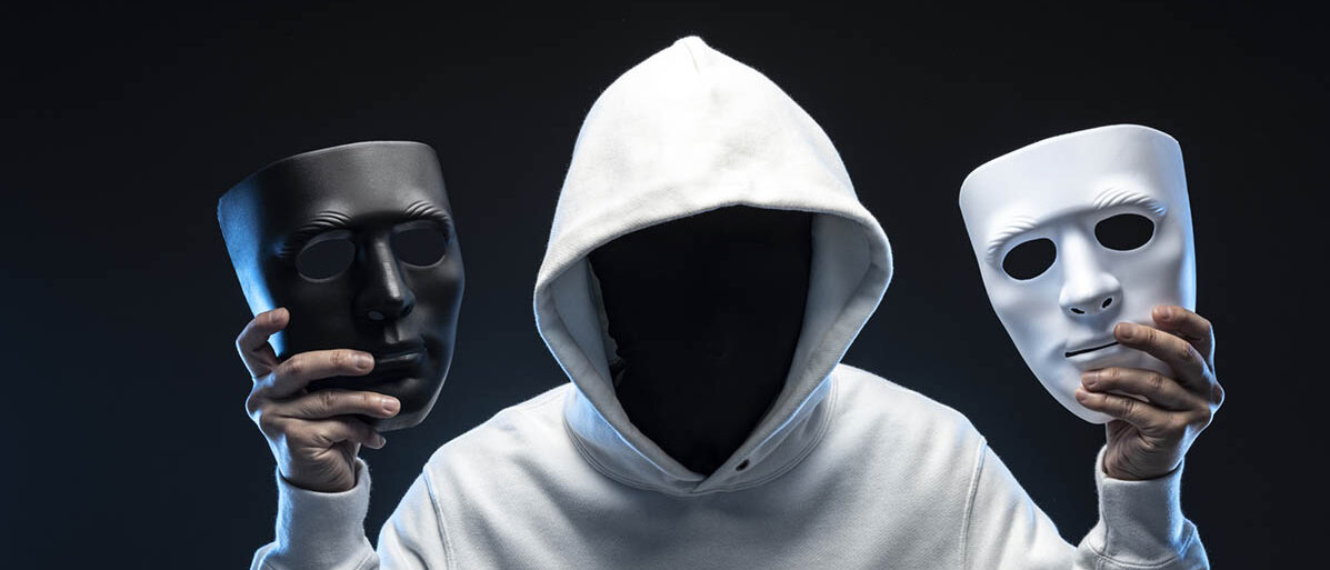 Persönlichkeitsstörung Psychopathie: Ursachen, Merkmale, Therapie Ein Mann in einem weißen Hoody vor schwarzem Hintergrund hält zwei Masken hoch. Sein eigenes Gesicht ist nicht erkennbar, eine Maske ist schwarz, eine ist weiß.