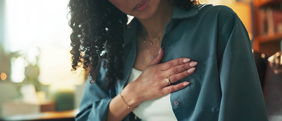 Sodbrennen und Reflux: Welche Mittel helfen? Was ist in der Schwangerschaft zu beachten und was ist von Hausmitteln zu halten? Eine Frau hat die Hand auf die Brust gelegt, sie ist leicht gekrĂŒmmt und schaut seitlich nach unten.