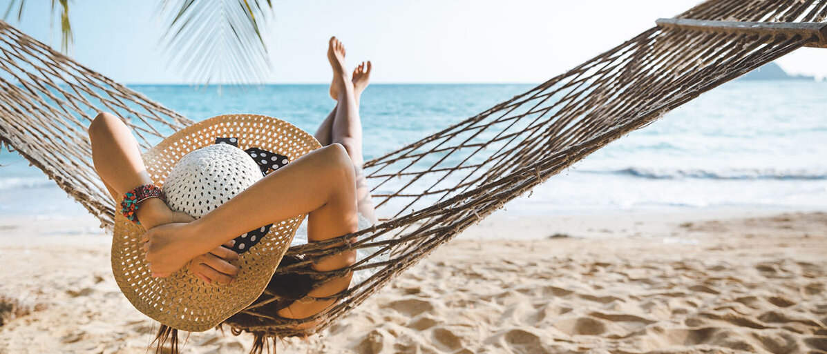 Urlaub genießen Frau mit Strohhut entspannt in einer Hängematte am Strand