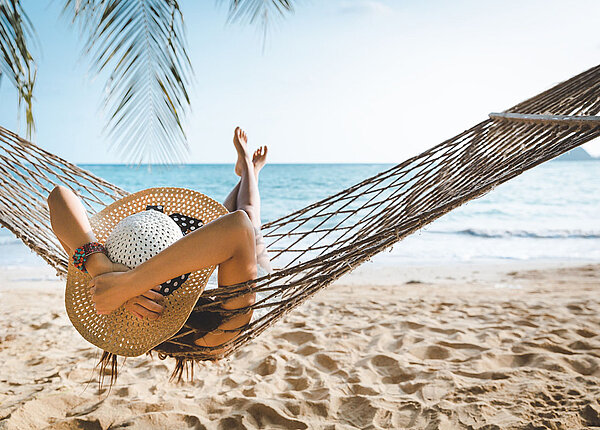 Urlaub genießen Frau mit Strohhut entspannt in einer Hängematte am Strand