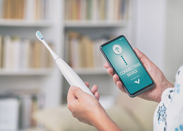 Eine elektrische Zahnbürste verbindet sich gerade mit einer App auf dem Smartphone 
