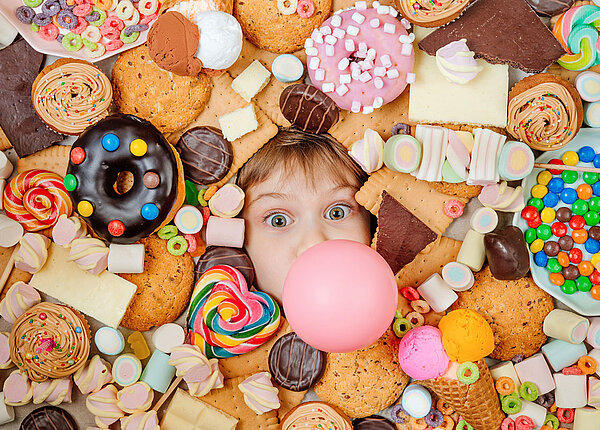 Kind schaut zwischen lauter Süßigkeiten mit seinem Kopf hervor