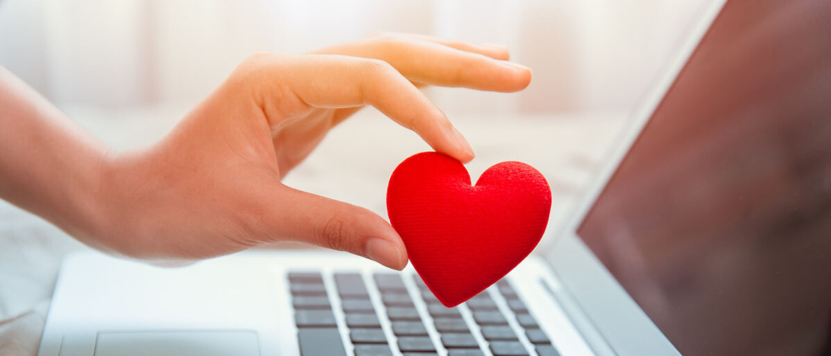 Frauenhand hält rotes Herz über Laptoptastatur 