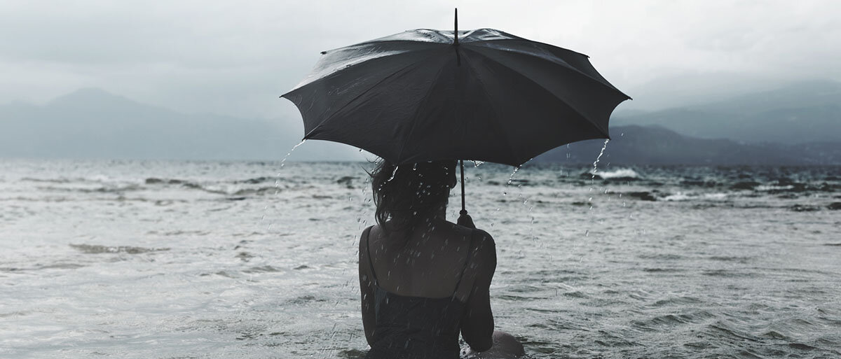 Eine Frau steht bis zum Bauch im Meer und hält einen Regenschirm.