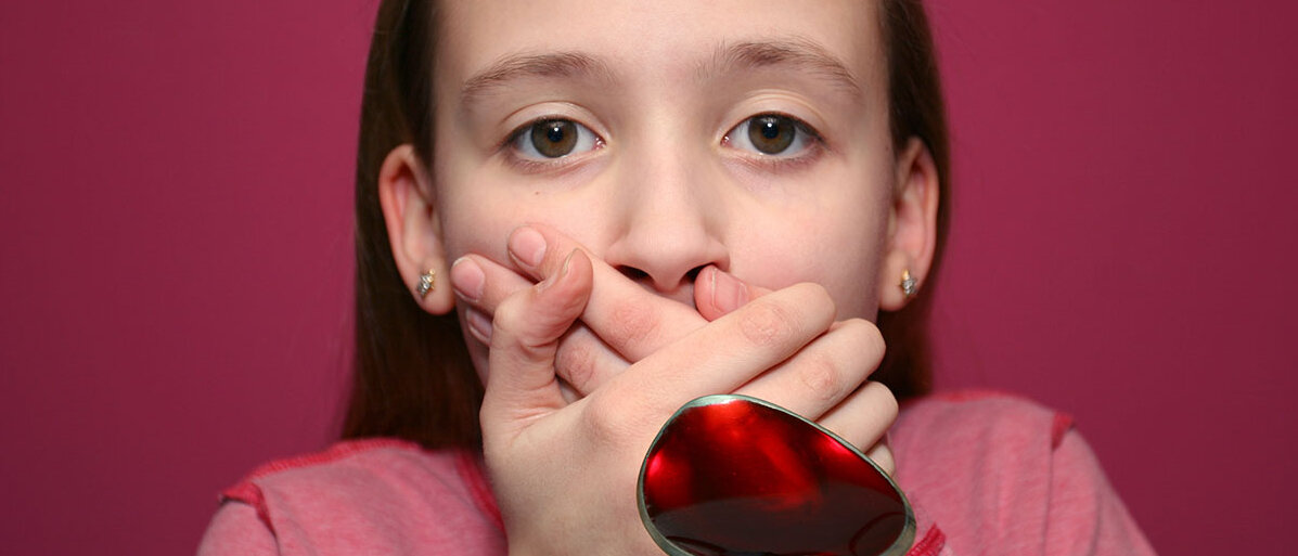 Ein Mädchen bekommt einen Löffel mit pinkem Saft vor den Mund gehalten, sie soll den Saft einnehmen. Aber das Mädchen hält sich mit beiden Händen den Mund zu.