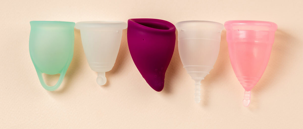 fünf Menstruationstassen, die sich in Farbe, Größe, Form und Rückholgriff unterscheiden