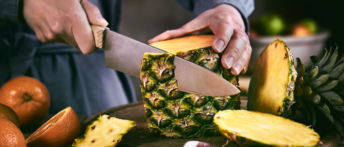 Mann schneidet mit großem Messer Schale einer Ananas ab