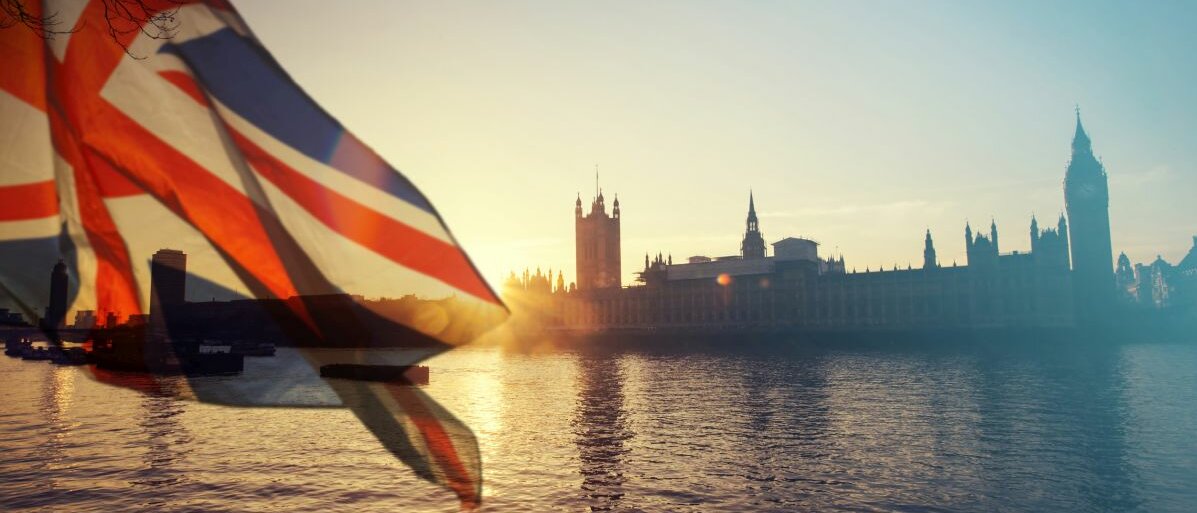 Die Ansicht über die Themse auf den Big Ben in London bei Sonnenuntergang und einer Großbritannien-Flagge im Vordergrund.