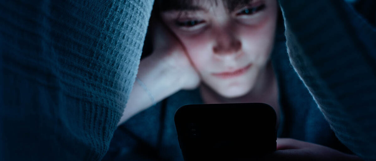 Eine Jugendliche nutzt ihr Smartphone nachts unter der Bettdecke.