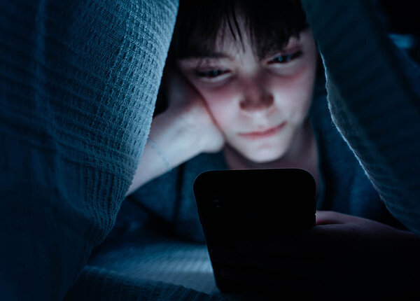 Sozialer Jetlag und dadurch zu wenig Schlaf begünstigt bei Jugendlichen Angst-Störungen. Eine Jugendliche nutzt ihr Smartphone nachts unter der Bettdecke.