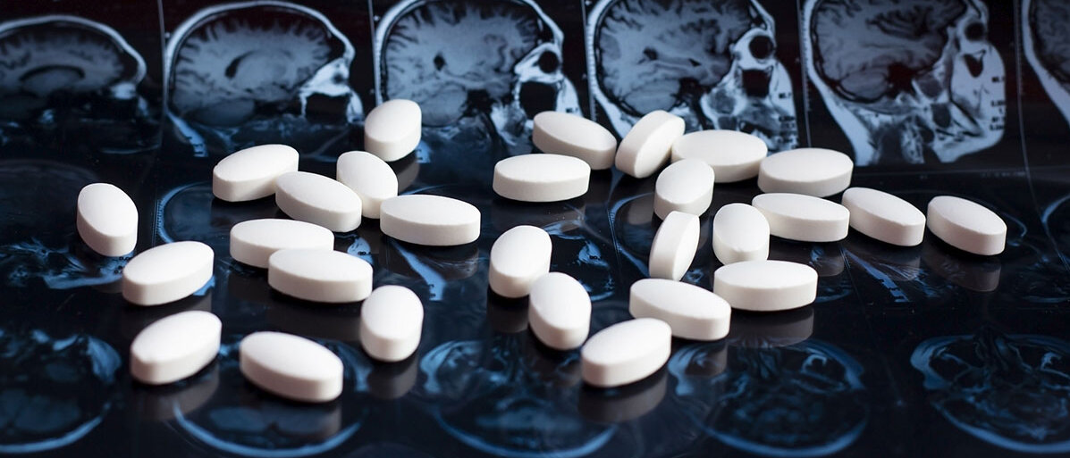 weiße Tabletten liegen vor einem Gehirn-Röntgenbild