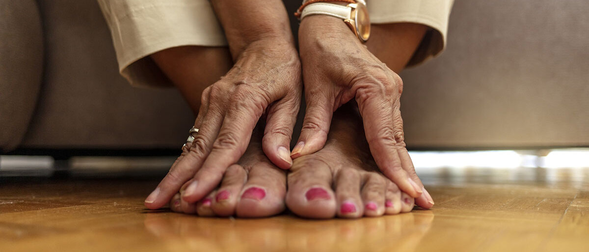 Eine ältere Frau massiert sich mit den Händen die Füße.