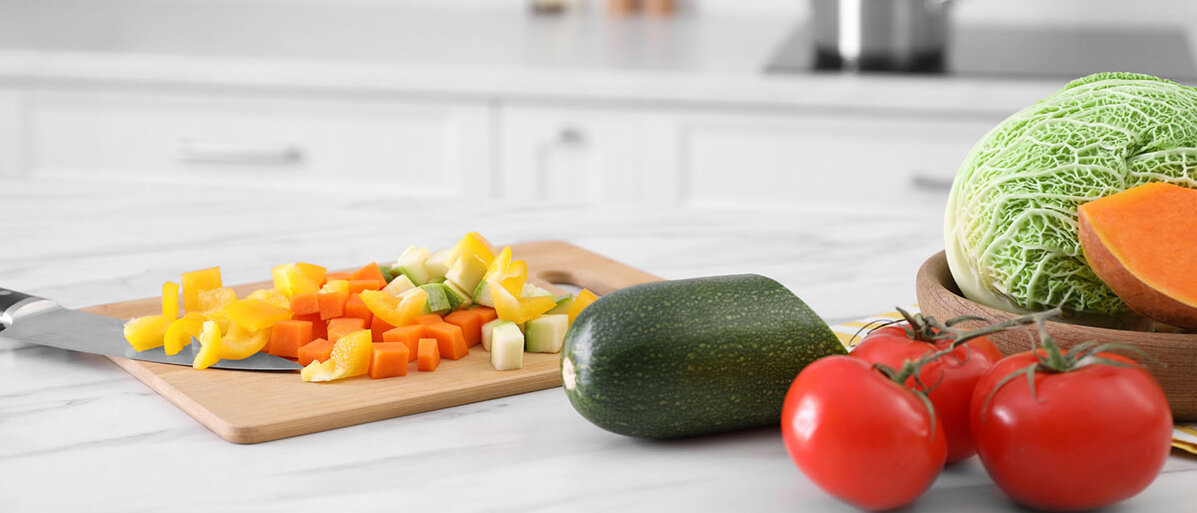 Küche richtig reinigen Verschiedenes Gemüse auf einem Schneidebrett in der Küche, daneben weiteres Gemüse.