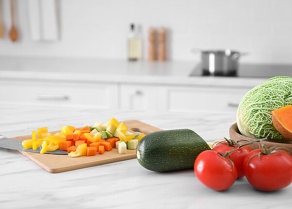 Küche richtig reinigen Verschiedenes Gemüse auf einem Schneidebrett in der Küche, daneben weiteres Gemüse.