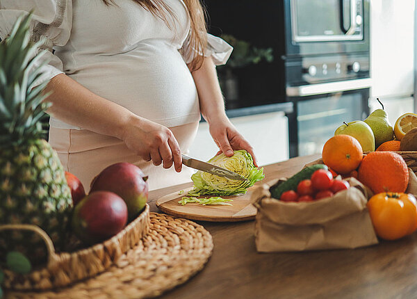 Ernährung in der Schwangerschaft Schwangere Frau schneidet Salat in der Küche