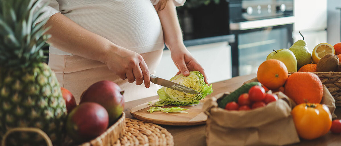 Ernährung in der Schwangerschaft Schwangere Frau schneidet Salat in der Küche