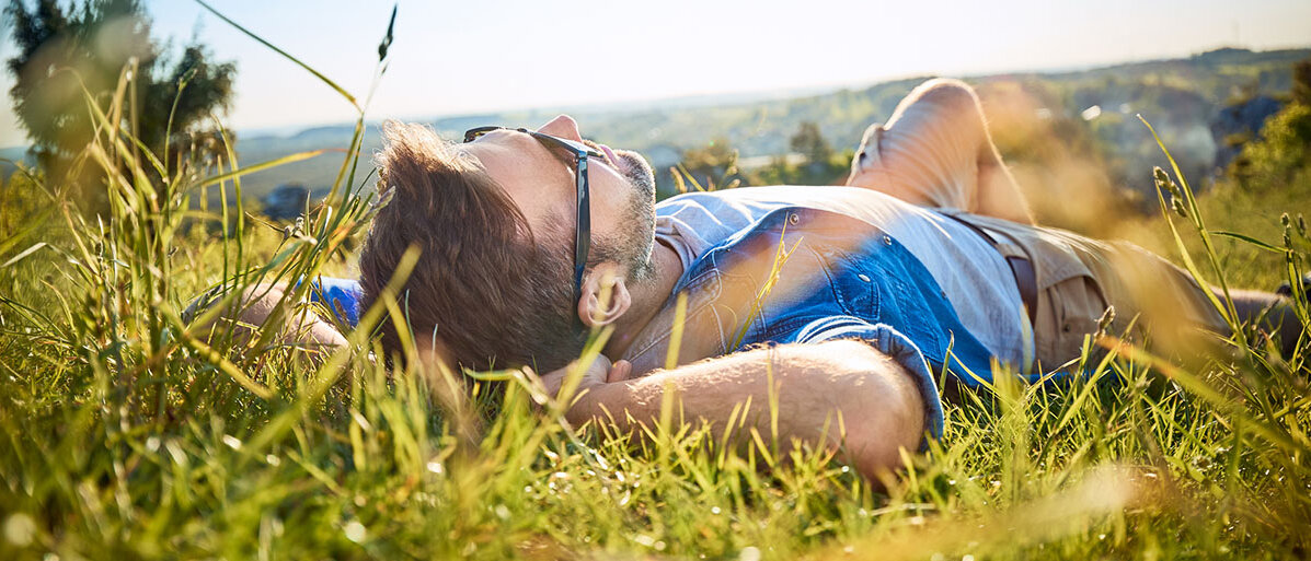 Mann liegt auf einer Wiese und traegt eine Sonnenbrille