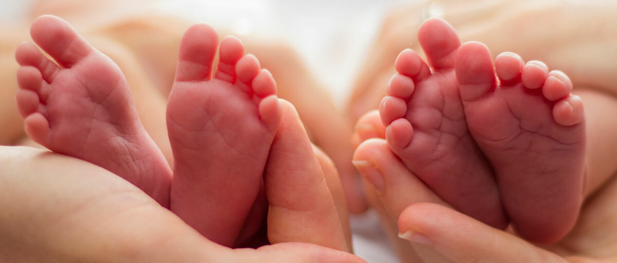 Zwei Personen halten jeweils ein Paar Babyfüße in den Händen.