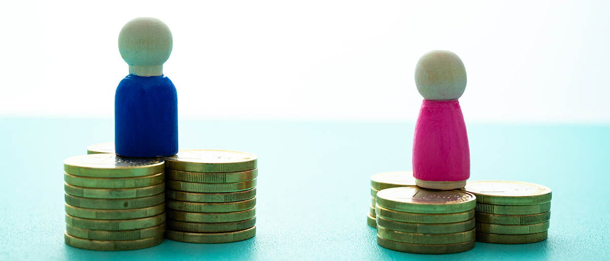 Gender Pay Gap bei den Gesundheitsberufen: Gehalt und Vedienst von Männern wesentlich höher als von Frauen Ein blaues Holzmännchen steht auf einem höheren Münzstapel als ein rosa Holzfigürchen.