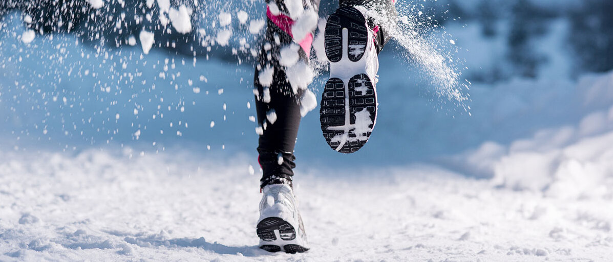 Frauenbeine joggen auf Schnee und hinter ihr spritzt der Schnee hoch
