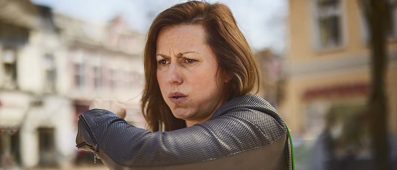 Eine Frau befindet sich draußen und hustet in ihre Armbeuge