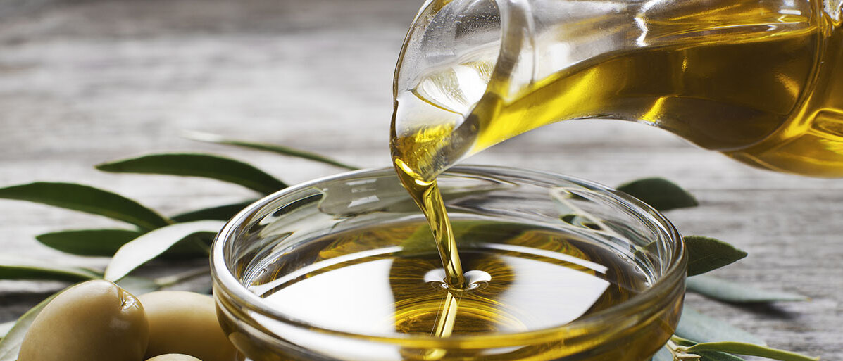Olivenöl wird in eine Schlüssel gegossen. Nebendran liegen grüne Oliven
