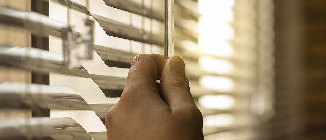 Hitzeschutz-Tipps Eine Hand macht den Rollo an einem Fenster zu