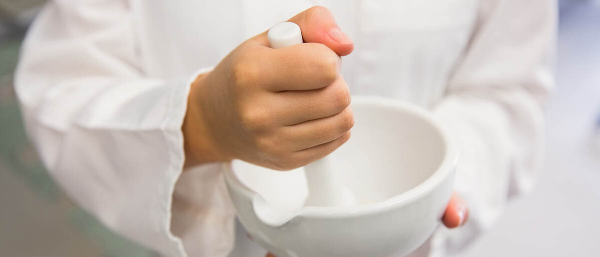 Eine Person in weißem Kittel rührt mit einem Pistill in einer Fantaschale.