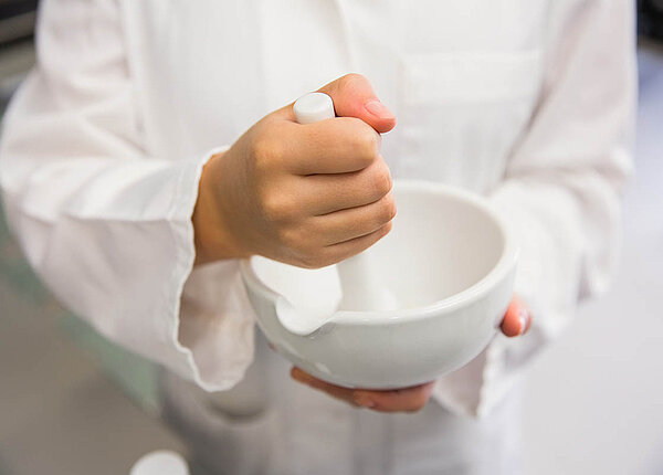 Salben herstellen: Theorie zu Salbengrundlagen, Lösungssalben und Suspensionssalben Eine Person in weißem Kittel rührt mit einem Pistill in einer Fantaschale.