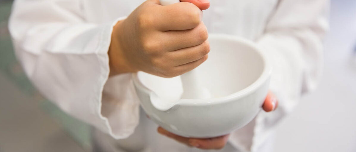 Salben herstellen: Theorie zu Salbengrundlagen, Lösungssalben und Suspensionssalben Eine Person in weißem Kittel rührt mit einem Pistill in einer Fantaschale.