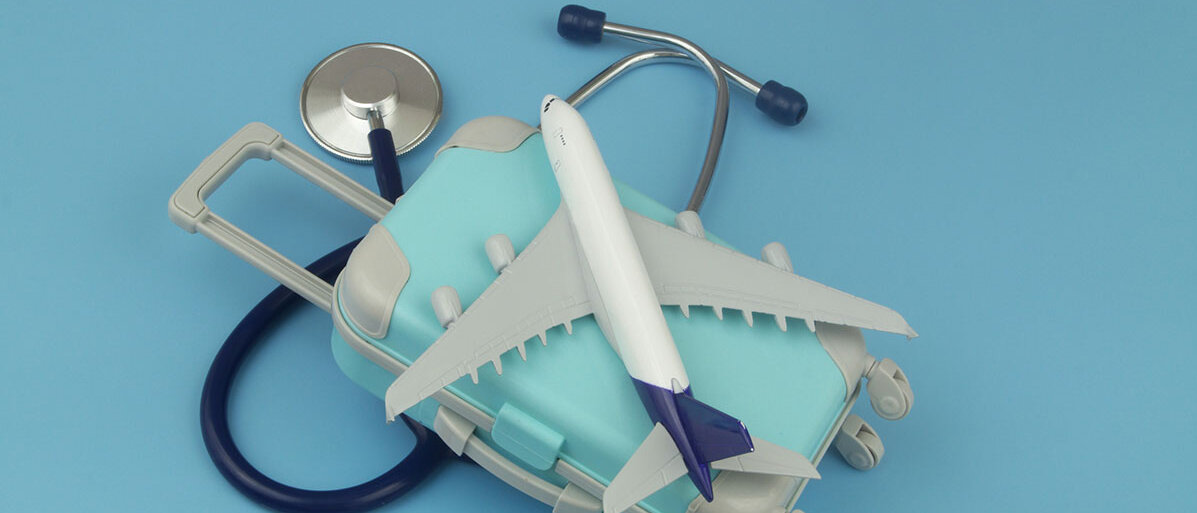Flugzeug und Koffer liegen auf Stethoskops auf blauem Hintergrund