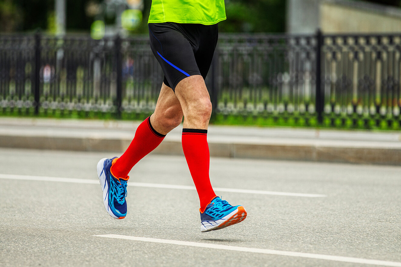 Jogger läuft über die Straße mit roten Kniestrümpfen 
