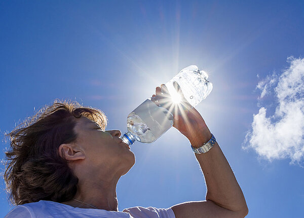 Frau trinkt in der Sonne eine Flasche Wasser bei Sonnenstrahlen