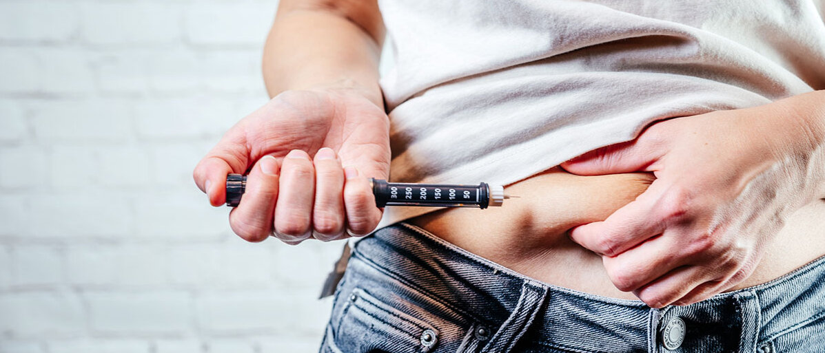 Eine Frau injiziert Insulin mit einem Pen in das Unterhautgewebe ihres Bauches.