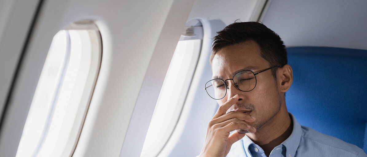 Mann sitzt im Flugzeug am Fenster und hat die Augen geschlossen