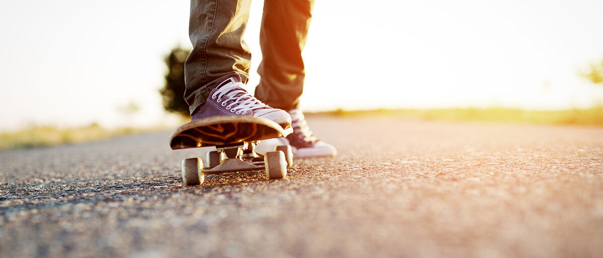 Eine Person stößt sich mit einem Fuß von einer asphaltierten Straße ab, um zu skateboarden.