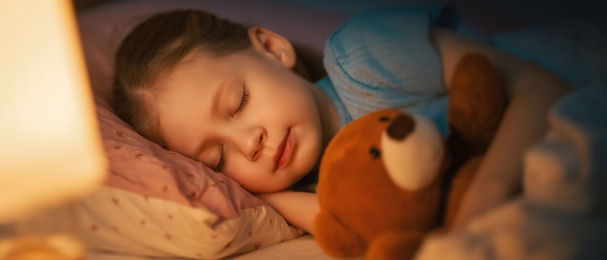 Kind mit Teddybär liegt im Bett und schlaeft