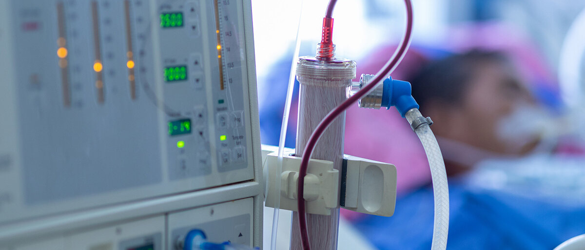Im Vordergrund eine Dialysemaschine, im Hintergrund unscharf ein Patient