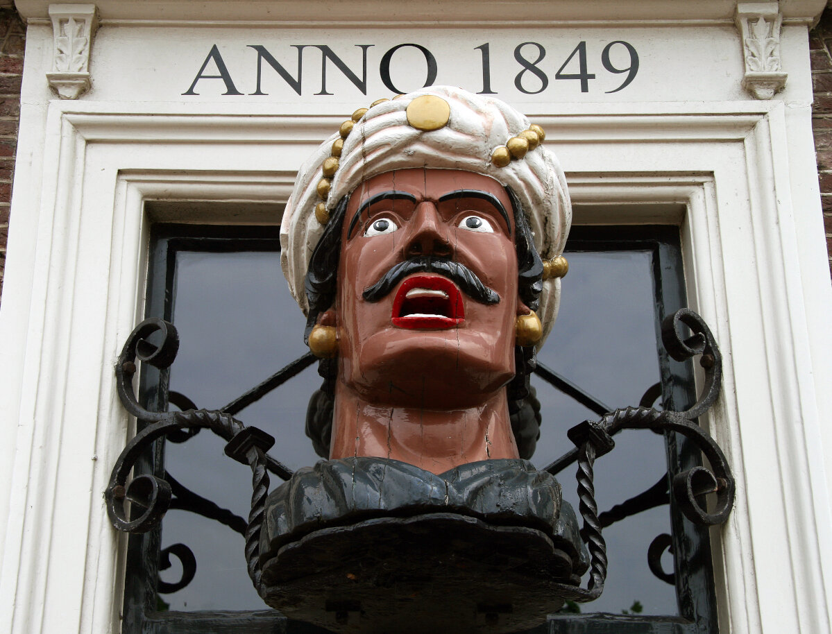 Ein sogenannter Gaper an der Fassade einer niederländischen Apotheke: Der geschnitzte Holzkopf hat den Mund geöffnet, um ein Medikament einzunehmen. Auf der Fassade ist außerdem „Anno 1849“ zu lesen.