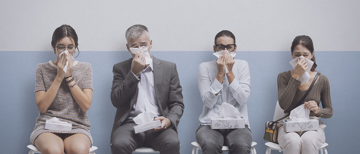 Vier Menschen mit Schnupfen warten auf Stühlen