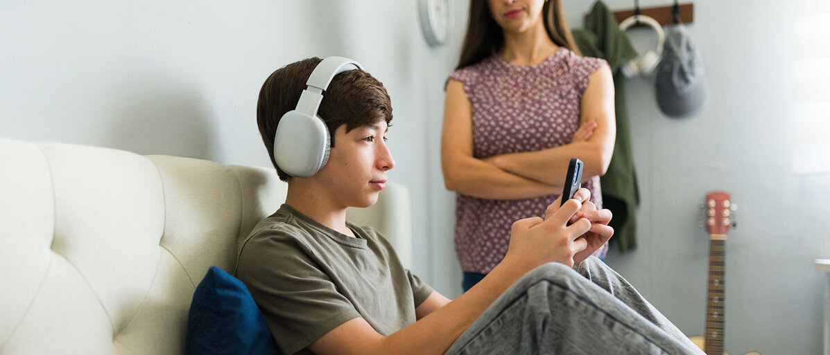 Social Media für Jugendliche Teenager ignoriert Mutter, während er mit dem Handy auf dem Bett sitzt