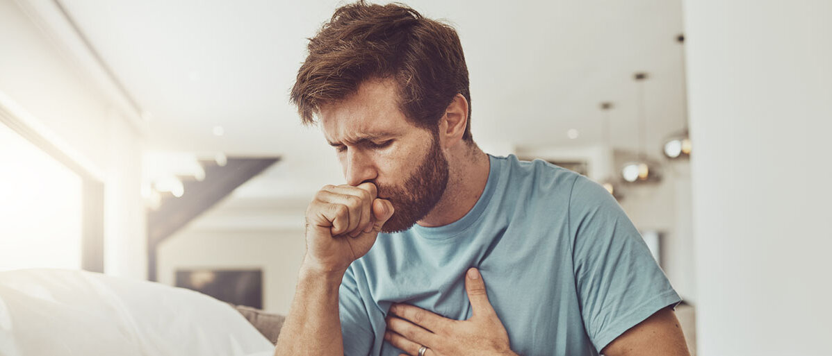 Hustender Mann fasst sich an die Brust 