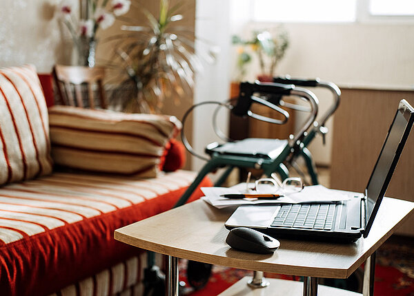 Stürze mit Rollator vermeiden Wohnzimmer mit Sofa, Couchtisch und Laptop, im Hintergrund ein Rollator
