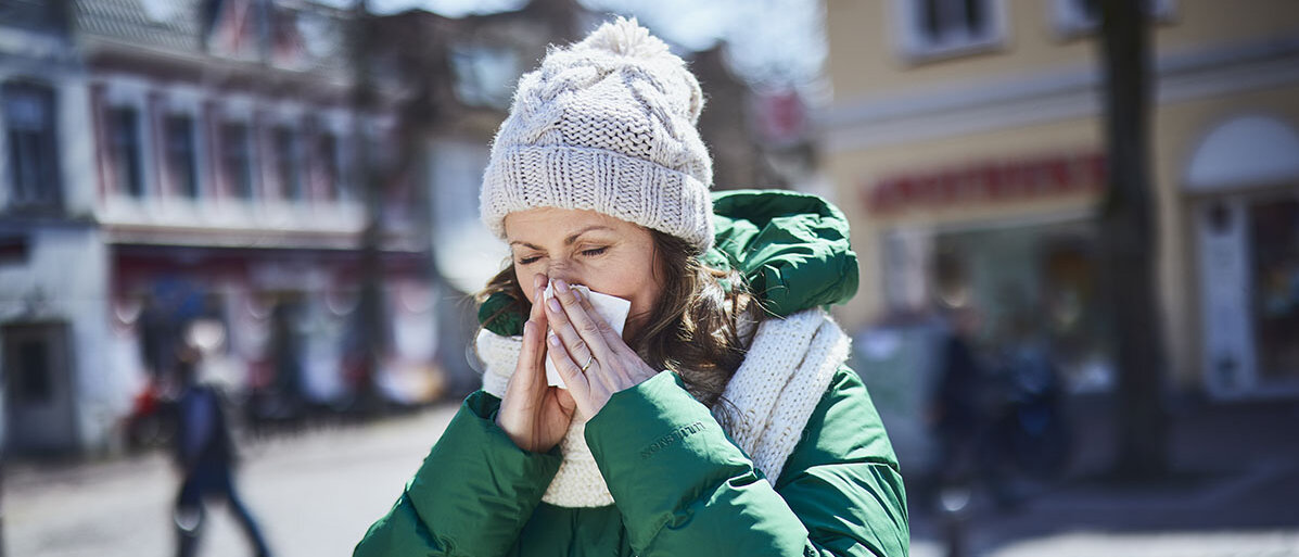 Frau mit grüner Jacke schneuzt in ein Taschentuch