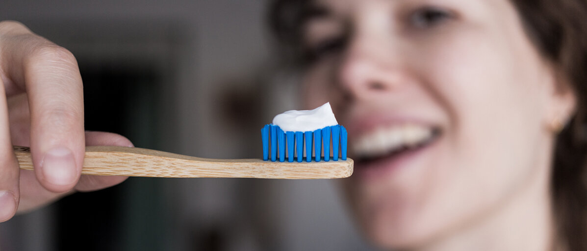 Eine Frau hält eine Holzzahnbürste mit Zahnpasta in den Vordergrund