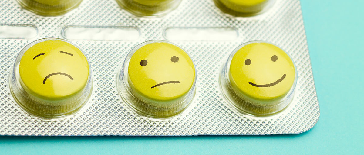 Gelbe Pillen mit aufgemalten Gesichtern in einem Blister auf blauem Grund.